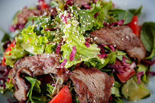 Grilled veal slices salad with romaine lettuce, spinach and tomato chops, sesame seed on top, served in plate, close-up
