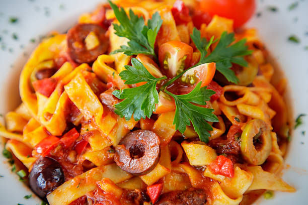 Pasta tagliatelle in red sauce with sliced olives, cherry tomato and parsley on top served in deep plate, close-up
