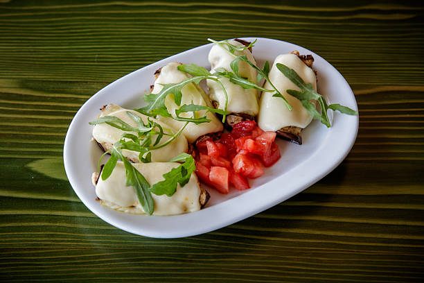 Chicken white meat rolled in eggplant slices and melted cheese, served with arugula and chopped tomato in plate on the table