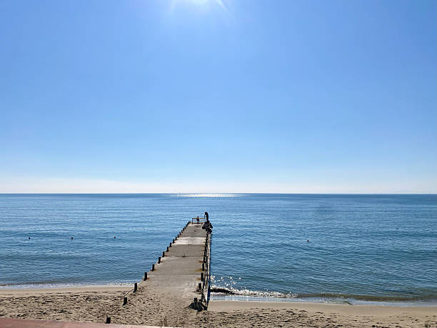 Scenic wooden pier stretches into serene blue sea, bathed in sunlight, creating a peaceful atmosphere perfect for relaxation and contemplation