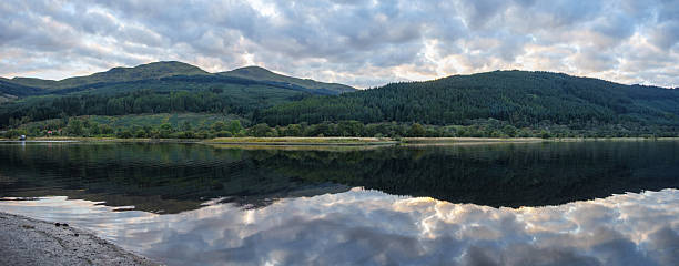 Serene loch fyne landscape showing tranquil water perfectly reflecting the dramatic cloudscape and distant tree-covered mountains of the scottish highlands