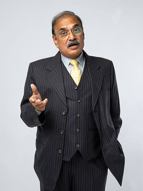 Elderly businessman in formal suit and glasses showing stop sign with shocked expression on white background