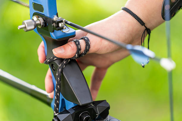 Archer in a lush green setting preparing a compound bow with a steady grip, showing concentration and readiness for a precise shot.