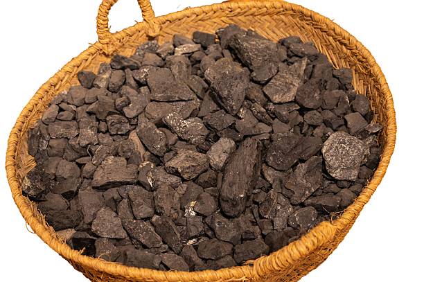 Raw mine coal chunks filling a traditional esparto woven basket, isolated on a clean white background. Focus on the contrasting texture and material.