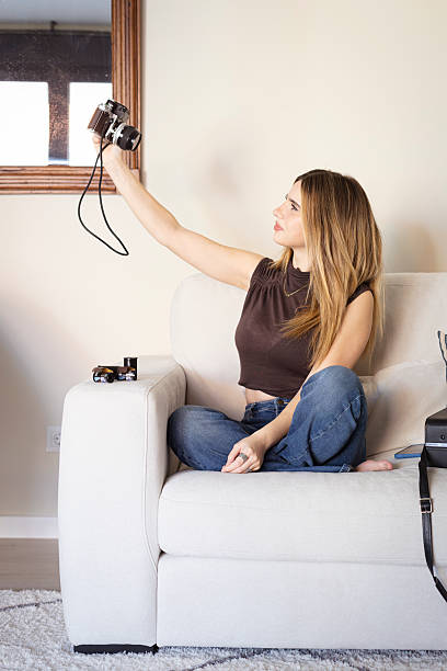 Young woman on a couch taking a self-portrait with an old film camera indoors