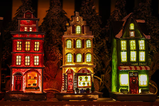 A beautifully lit trio of miniature Christmas village houses glows warmly against a dark, festive backdrop. The colourful windows and detailed façades create a cosy, magical holiday atmosphere, perfect for seasonal advertising, Christmas cards, editorial features, or winter-themed commercial projects.