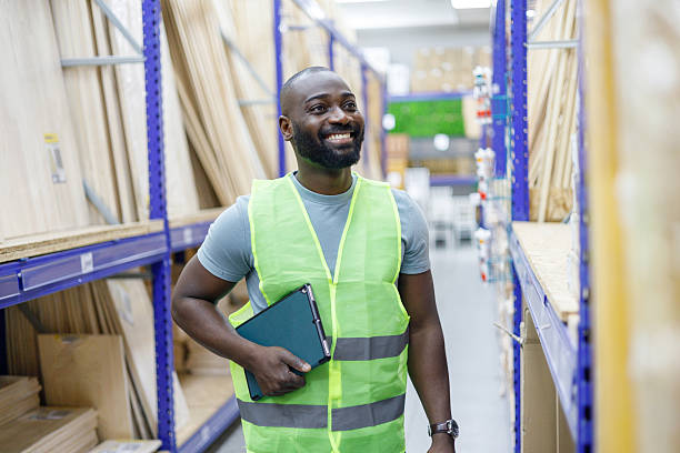 istock African american man warehouse worker smiling with inventory clipboard, looking up at commercial shelving aisle 2249314946