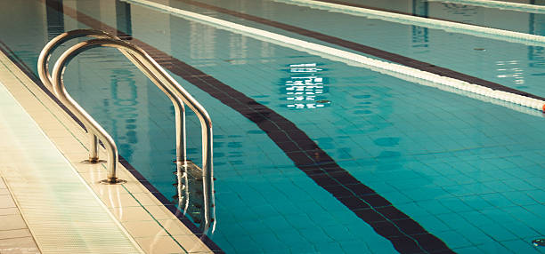 Senior adult man wearing a swimming cap and goggles, stretching his arms in an indoor swimming pool, enjoying recreation and health benefits of water exercise
