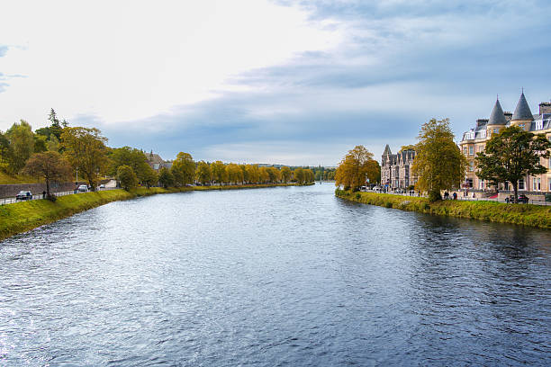River ness flowing through the scenic city of inverness, scotland, lined with historic buildings and vibrant autumn trees under a cloudy sky, showcasing urban landscape and natural beauty