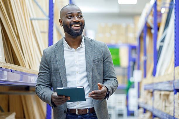 istock Confident black male manager smiling, holding a digital tablet while checking stock in a modern retail warehouse 2249317953