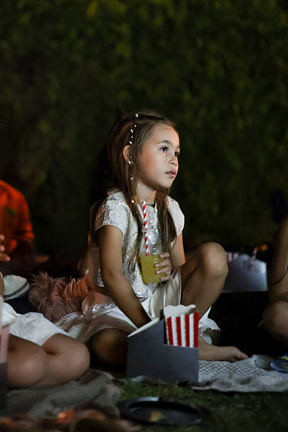 Group of children are sitting in the yard during a birthday party and watching a movie on a video projector