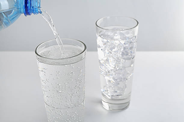 istock Pouring refreshing soda water into glass at white table against light background 2249321073