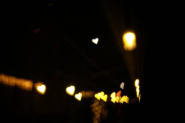 Romantic decor. Blurred view of heart shaped lights on black background, bokeh effect