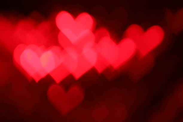 Romantic decor. Blurred view of heart shaped lights on dark red background, bokeh effect