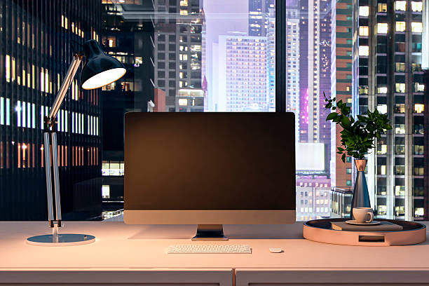 istock Modern desktop computer on clean office desk with lamp and city window view at night, blank screen for mockup or design template. 3D Rendering 2249322906