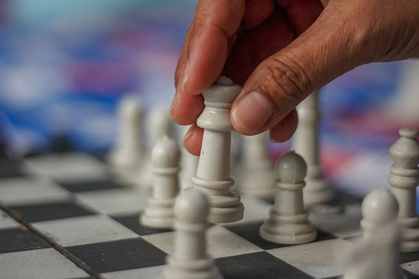 person moving a white chess piece, on a chessboard.