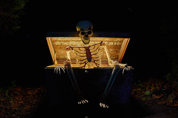 Skeleton figure sitting in open chest illuminated at night. Concepts of Halloween, decoration, spooky themes and seasonal events