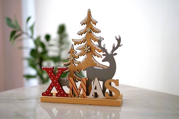 Wooden Christmas decor featuring a tree and reindeer placed on a marble surface with a plant in the background