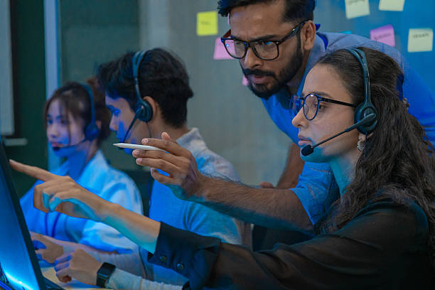 istock Customer support team in a modern call center receiving guidance from a supervisor. Diverse employees working with headsets and computers, representing teamwork, communication, and business technology. 2249341799