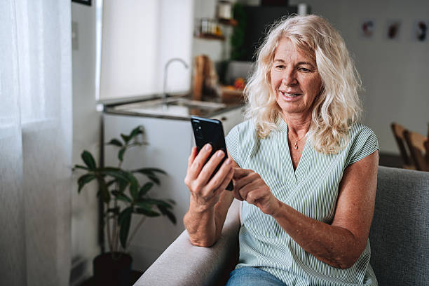 istock Happy senior woman smiling while using smartphone at home 2249343035