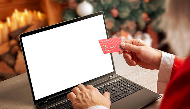 istock Santa holding credit card while using laptop with blank screen in warm Christmas interior, ideal for holiday mockups, ecommerce concepts and festive digital marketing 2249343177