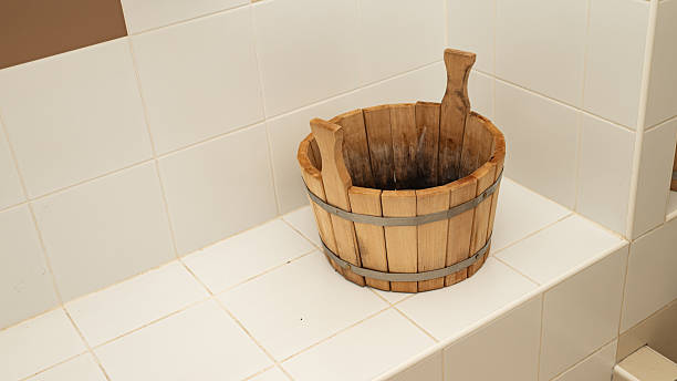 Wooden bucket with handles on white tiled bathroom surface.