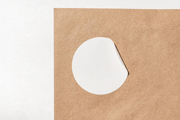 istock White circle sticker partially peeled on brown paper surface 2249343869