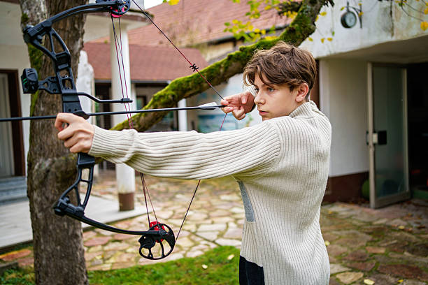 Teenage boy practicing archery with bow and arrows outdoors. Young male learning traditional sport activity, focus and concentration. Real life, real people lifestyle concept