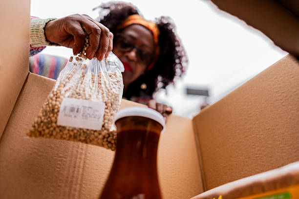 A detailed close-up shot capturing the hands of a volunteer carefully placing a packaged food item into a cardboard box, highlighting the personal touch of community support and charitable giving.