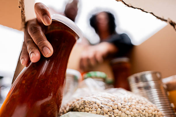 A detailed close-up shot showing a volunteer carefully placing a food jar into a cardboard box, highlighting the personal connection and commitment to community support and charitable giving.