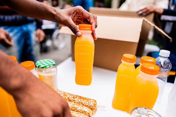 A detailed close-up view of a volunteer's hand organizing orange juice bottles during a food donation preparation process, showcasing community support and humanitarian efforts.