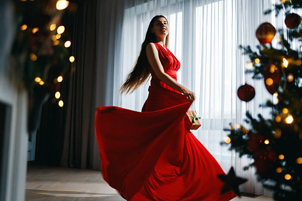 Happy young beautiful woman near Christmas tree indoor.