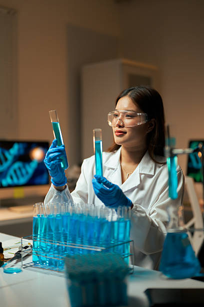 Female scientist wearing gloves and safety glasses holding test tubes with blue liquid, performing experiments in a science laboratory
