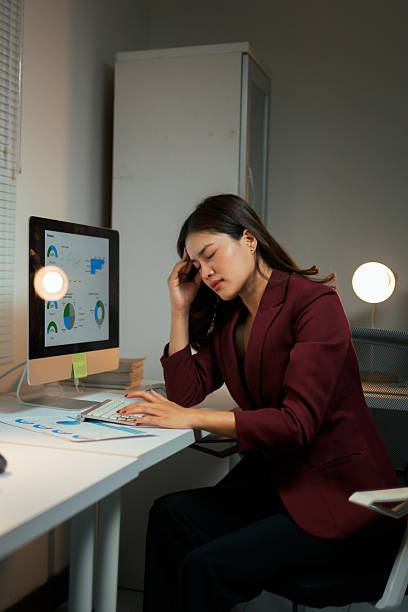 Young adult businesswoman feeling tired and stressed, having a headache while working late at night in an office on a computer