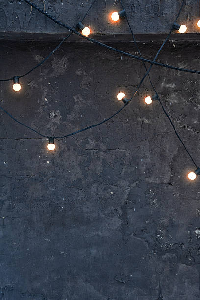 istock Glowing string lights on a dark concrete wall create a moody and cozy ambiance. Industrial textured background perfect for minimalist and trendy designs 2249360271