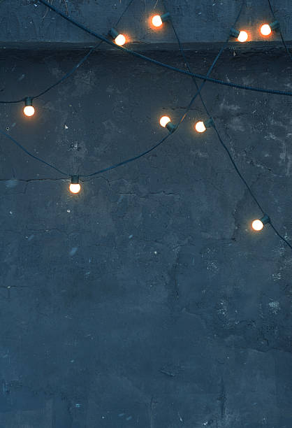 istock Glowing string lights on a dark concrete wall create a moody and cozy ambiance. Industrial textured background perfect for minimalist and trendy designs 2249360300