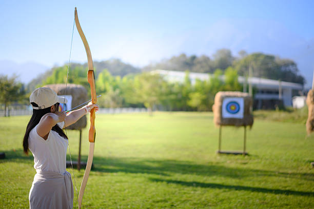 Woman practicing archery at straw targets outdoors.
