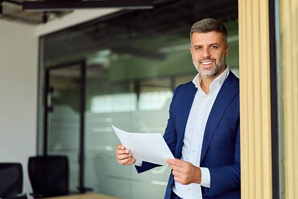 istock Confident Businessman In Blue Suit Smiles While Holding Documents At Office Entrance Door 2249367901