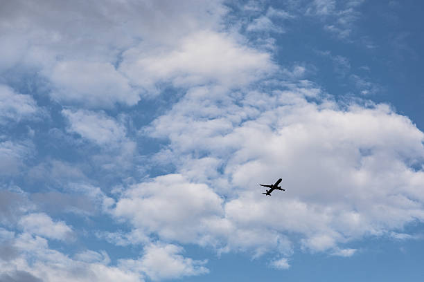 istock Airplane silhouette flying through blue sky with white fluffy clouds 2249367911