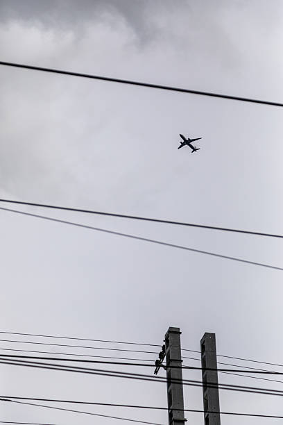 istock Airplane silhouette flying between power lines and utility poles in gray sky 2249368669