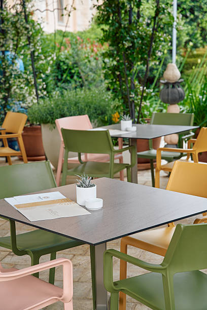 istock Charming Outdoor Dining Area Surrounded by Lush Greenery Featuring Colorful Chairs and Modern Tables for Relaxing Meals and Social Gatherings 2249369284