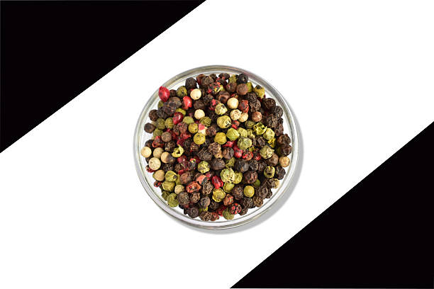 Peppercorns of different colors lie in a round vase. View from above.