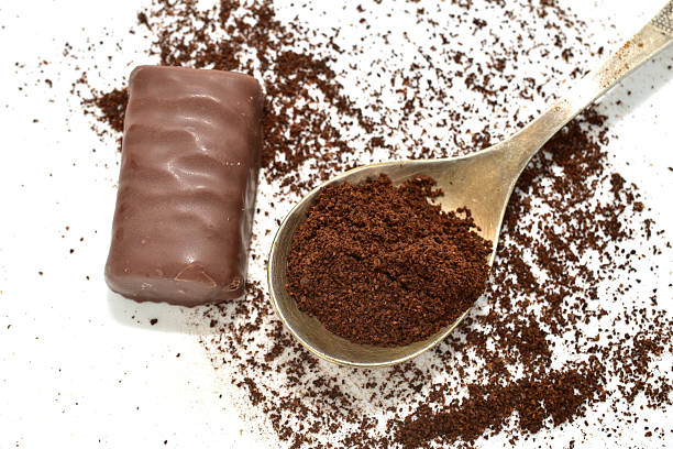 Ground black coffee lies in a spoon and on the surface of a white background.
