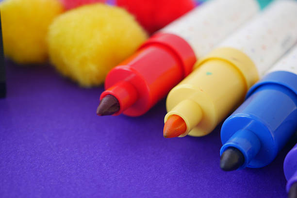 Bright markers and fluffy pom poms arranged on a vibrant background.
