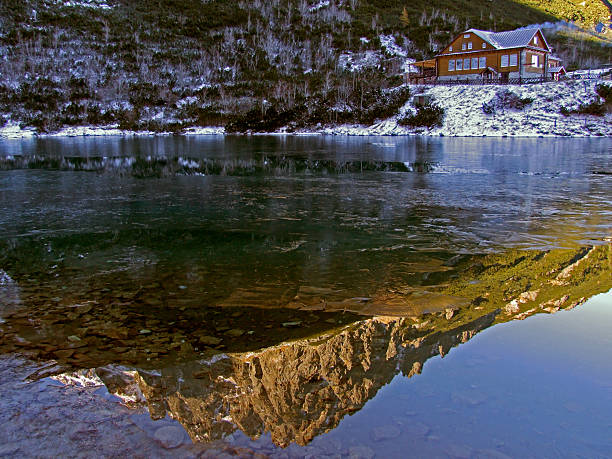 Cabin reflects in calm mountain lake.