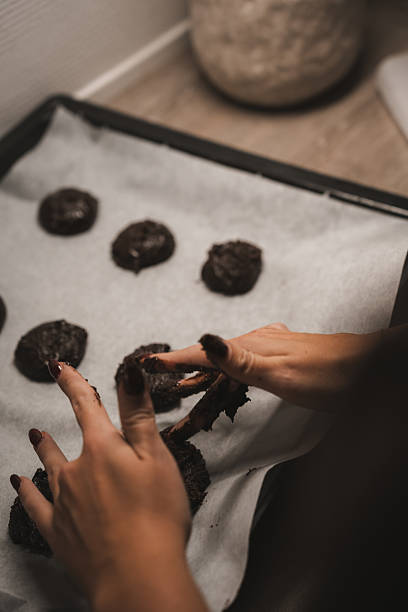istock Hands shape chocolate cookie dough on a baking tray lined with parchment paper in a warm kitchen. The soft lighting creates a comforting atmosphere, perfect for baking 2249373964