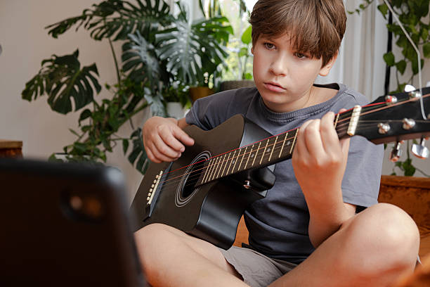 istock Young boy playing an acoustic guitar indoors, focused on pressing strings and fretboard 2249381991