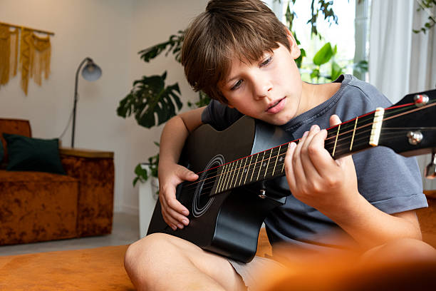istock Young boy playing an acoustic guitar indoors, focused on pressing strings and fretboard 2249381994