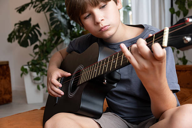 istock Young boy playing an acoustic guitar indoors, focused on pressing strings and fretboard 2249382000