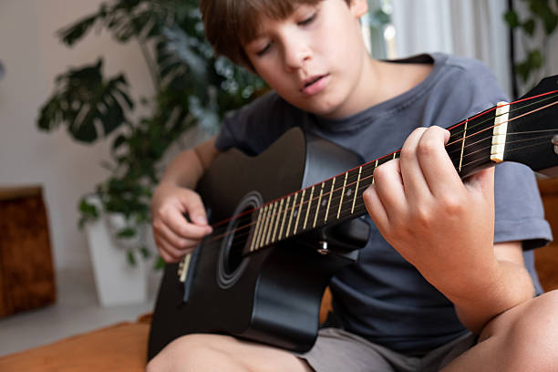 istock Young boy playing an acoustic guitar indoors, focused on pressing strings and fretboard 2249382010